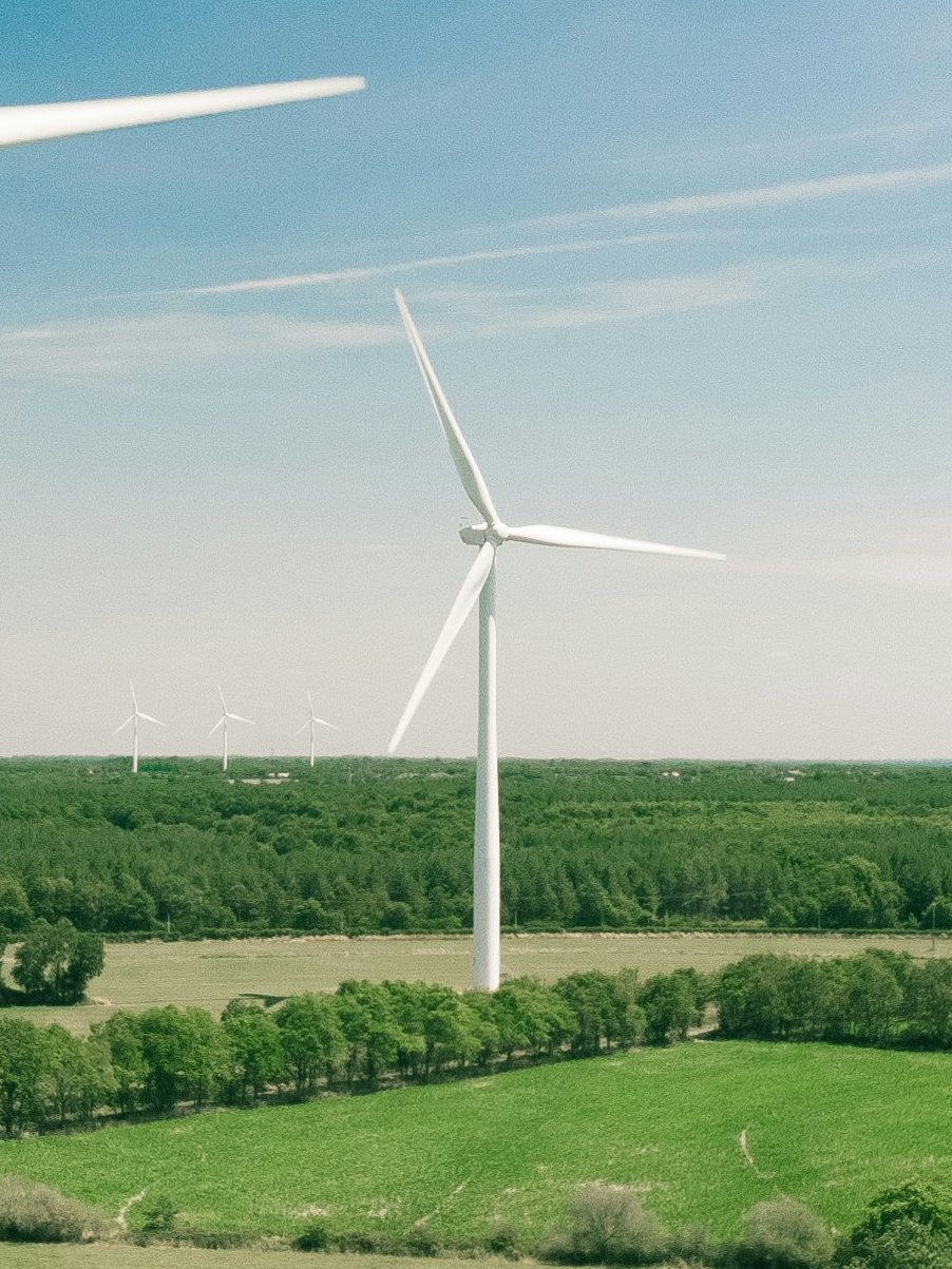 Windkraftanlagen in einer landwirtschaftlich genutzten Landschaft, Waldgebiete im Hintergrund.
